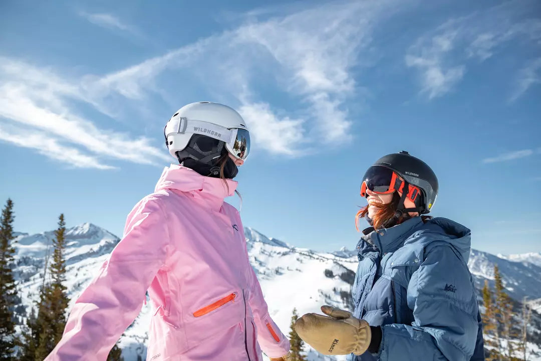 Two girls laughing with each other while skiing and wearing Wildhorn ski goggles